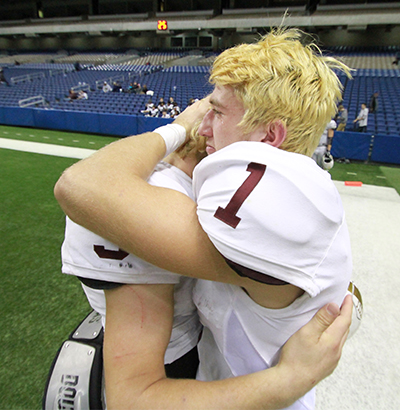 Dripping Springs Tiger senior running back Teo Brinckmann (1) sheds a tear as he embraces senior quarterback Reese Johnson following the team’s 51-28 loss to the Richmond Foster Falcons Saturday at the Alamodome in San Antonio. Dripping Springs’ finish in the state quarterfinals is the deepest by any Tiger team in school history. (photo by Moses Leos III)